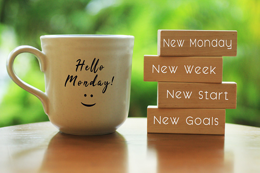 Hello Monday concept with inspirational motivational positive quote on wooden blocks - New Monday. New Week, New Start. New Goals. And a smiling face on a white morning cup of coffee or tea.